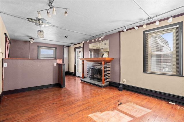 unfurnished living room with baseboards, a brick fireplace, wood finished floors, and track lighting