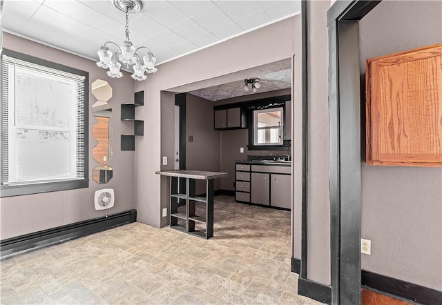 interior space with a textured wall, a baseboard radiator, a sink, and an inviting chandelier