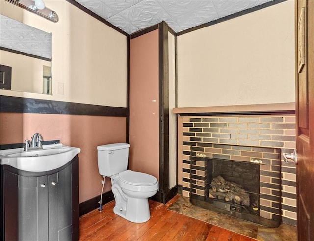 bathroom with an ornate ceiling, a fireplace, toilet, vanity, and wood finished floors