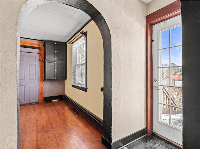 corridor featuring dark wood-style floors, arched walkways, a textured wall, and baseboards