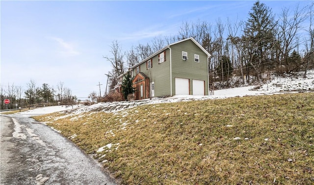 view of snow covered exterior featuring driveway, a lawn, and an attached garage