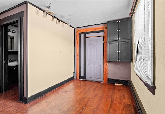 spare room featuring baseboards, a baseboard heating unit, dark wood finished floors, and a sink