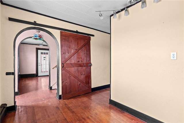 interior space with arched walkways, a barn door, baseboards, dark wood-style floors, and track lighting