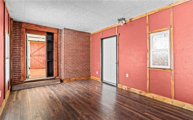 spare room featuring brick wall, dark wood finished floors, and a textured wall