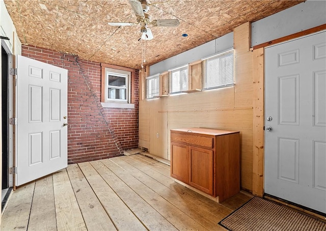 interior space featuring brown cabinets, light wood finished floors, light countertops, ceiling fan, and brick wall