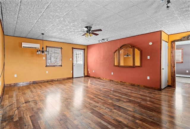 unfurnished living room featuring ceiling fan with notable chandelier, a wall mounted air conditioner, wood finished floors, and baseboards