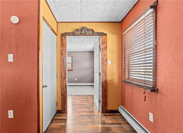 corridor featuring dark wood-style floors, baseboards, baseboard heating, and a textured wall