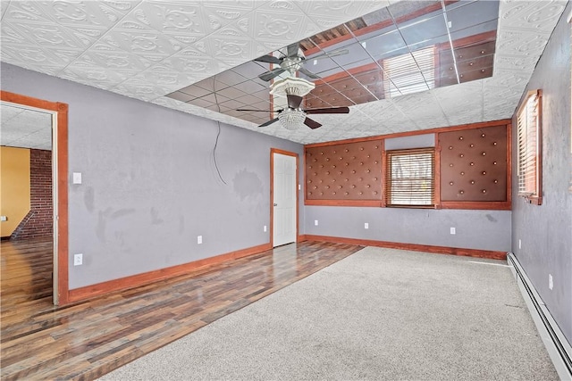 spare room with a baseboard heating unit, ceiling fan, wood finished floors, and baseboards