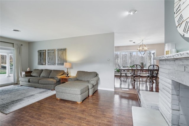 living room featuring a notable chandelier, a stone fireplace, and dark wood-type flooring