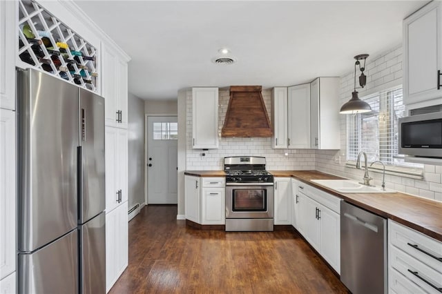 kitchen featuring wooden counters, appliances with stainless steel finishes, custom exhaust hood, sink, and pendant lighting