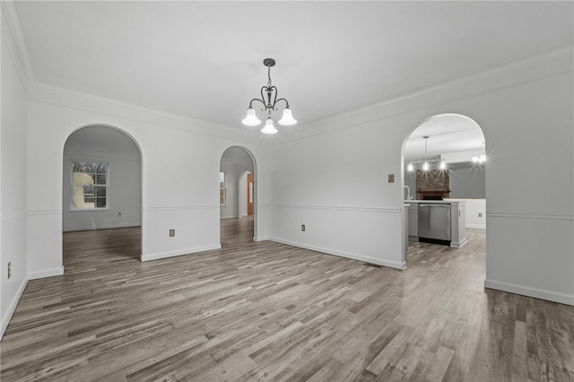 unfurnished living room featuring crown molding, light wood-type flooring, and an inviting chandelier