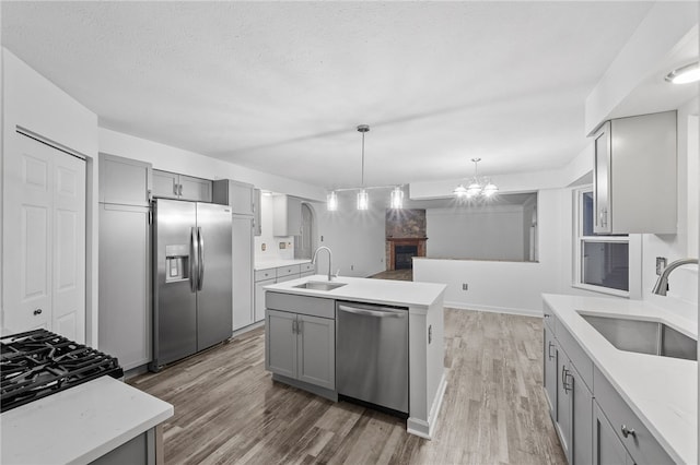 kitchen featuring appliances with stainless steel finishes, a kitchen island with sink, sink, a notable chandelier, and gray cabinets