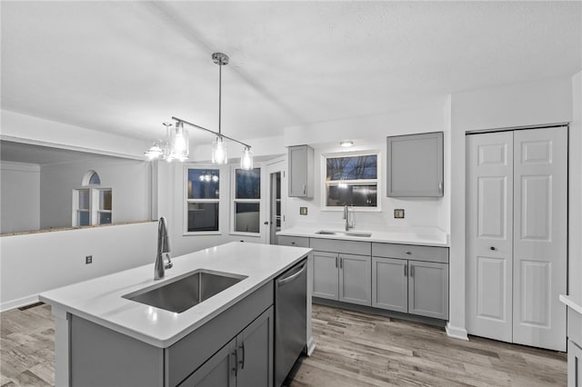 kitchen featuring a center island with sink, stainless steel dishwasher, gray cabinetry, and sink