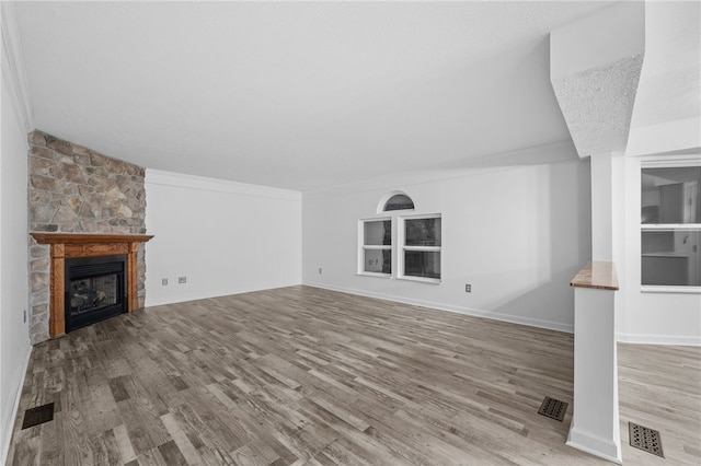 unfurnished living room featuring a stone fireplace, light hardwood / wood-style flooring, a textured ceiling, and ornamental molding