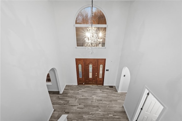 foyer entrance with hardwood / wood-style flooring, a towering ceiling, and a chandelier