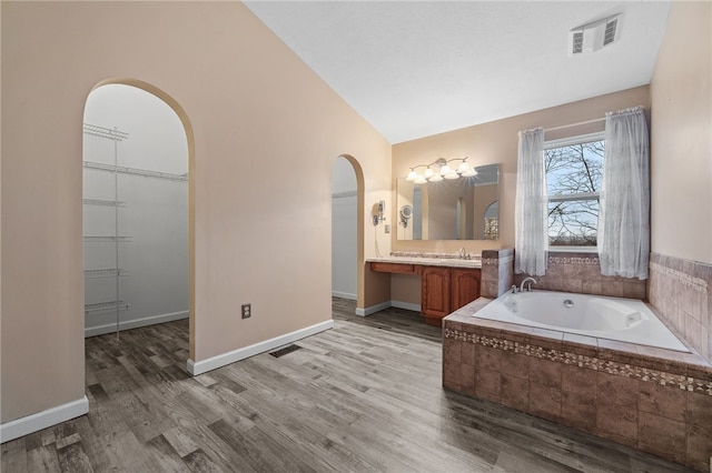 bathroom featuring wood-type flooring, vanity, tiled bath, and lofted ceiling