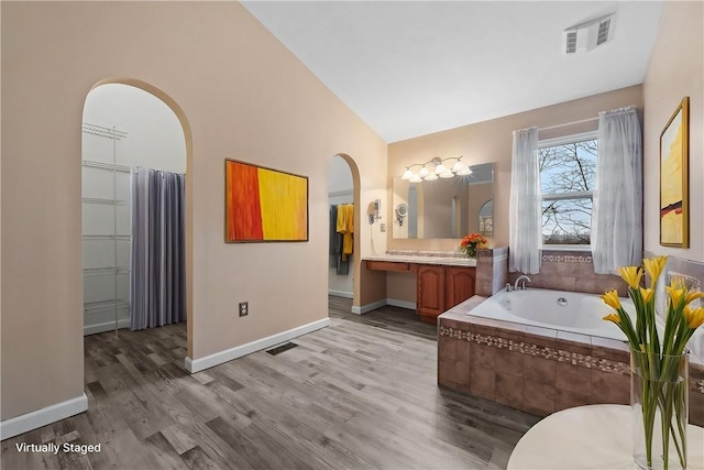 bathroom with hardwood / wood-style flooring, vanity, a relaxing tiled tub, and high vaulted ceiling