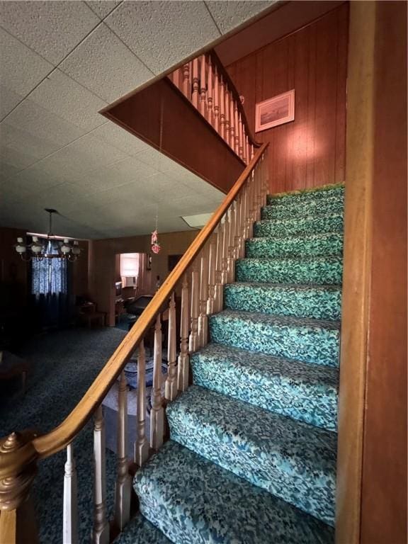 staircase featuring carpet, wooden walls, and a notable chandelier