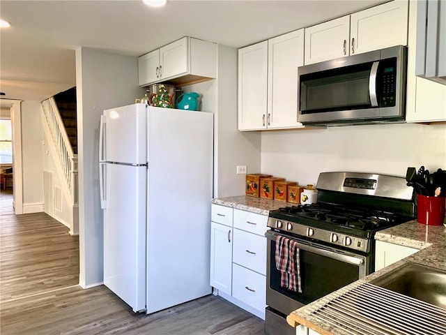 kitchen with light stone countertops, dark hardwood / wood-style flooring, white cabinets, and stainless steel appliances