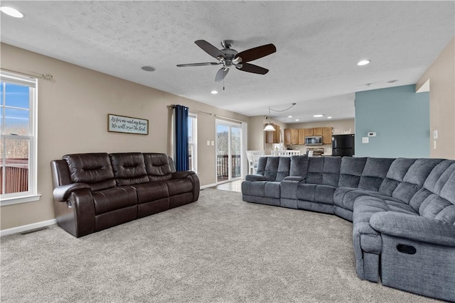 living room featuring a wealth of natural light, ceiling fan, light colored carpet, and a textured ceiling