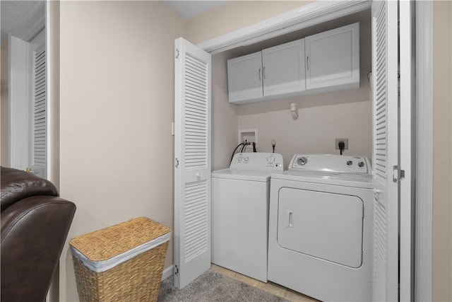 clothes washing area with washing machine and clothes dryer, light carpet, and cabinets