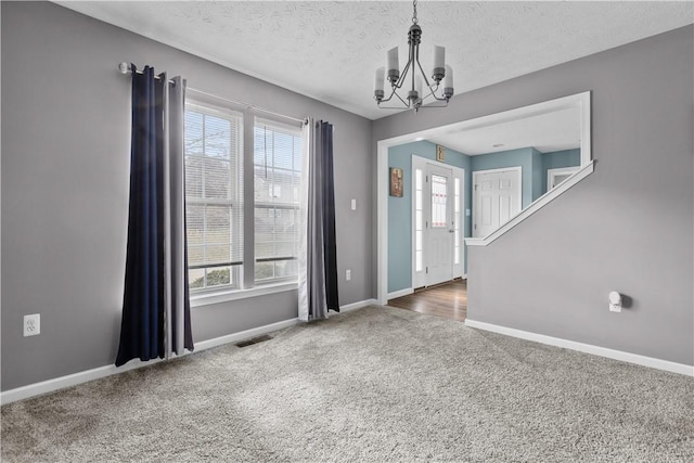 foyer entrance with carpet flooring, plenty of natural light, a textured ceiling, and an inviting chandelier