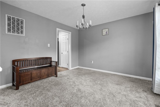 carpeted empty room with a textured ceiling and a notable chandelier