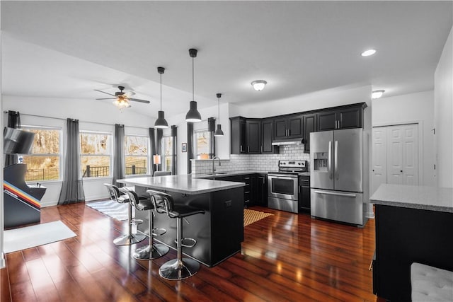 kitchen with a breakfast bar, a center island, sink, vaulted ceiling, and appliances with stainless steel finishes