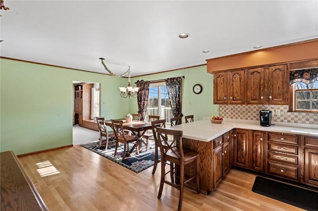 kitchen with hanging light fixtures, a notable chandelier, backsplash, kitchen peninsula, and light hardwood / wood-style floors