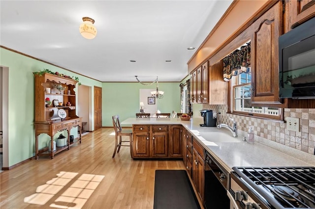 kitchen featuring sink, kitchen peninsula, light hardwood / wood-style floors, decorative light fixtures, and black appliances