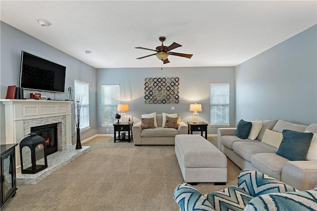 carpeted living room with ceiling fan and a stone fireplace