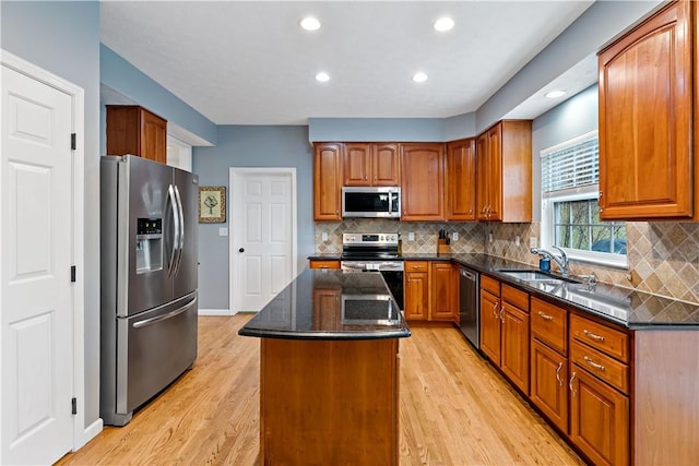 kitchen with appliances with stainless steel finishes, backsplash, sink, light hardwood / wood-style flooring, and a center island