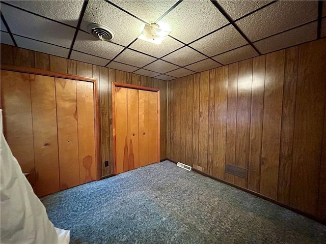 unfurnished bedroom with carpet, wooden walls, and multiple closets