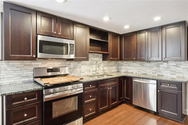 kitchen featuring light stone countertops, dark brown cabinets, stainless steel appliances, sink, and light hardwood / wood-style floors