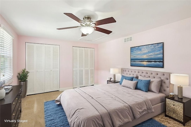 bedroom with light colored carpet, ceiling fan, and multiple closets