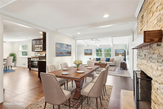 dining area featuring ceiling fan, a wealth of natural light, dark hardwood / wood-style flooring, beamed ceiling, and a fireplace