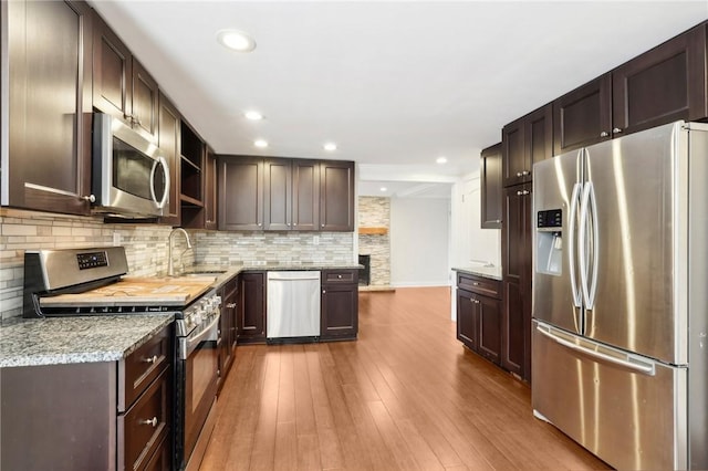 kitchen with backsplash, sink, light hardwood / wood-style flooring, light stone counters, and stainless steel appliances