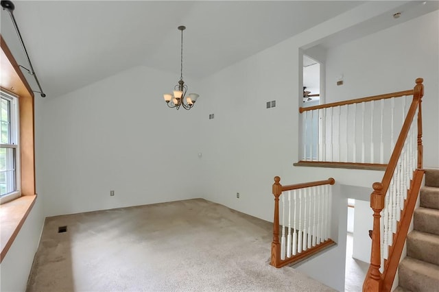 spare room featuring ceiling fan with notable chandelier, light colored carpet, and vaulted ceiling