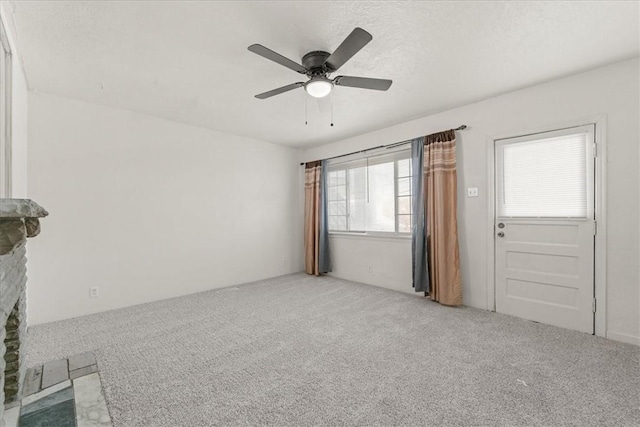 unfurnished room with ceiling fan, a fireplace, carpet, and a textured ceiling