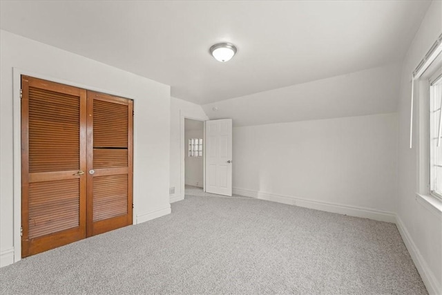 unfurnished bedroom featuring carpet, multiple windows, a closet, and lofted ceiling