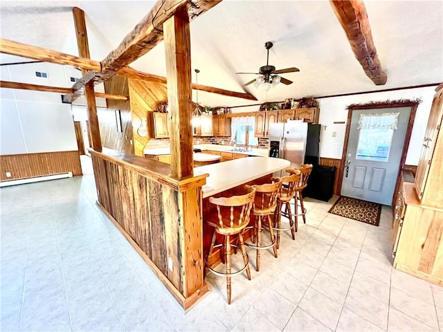 kitchen featuring ceiling fan, sink, baseboard heating, wood walls, and a breakfast bar