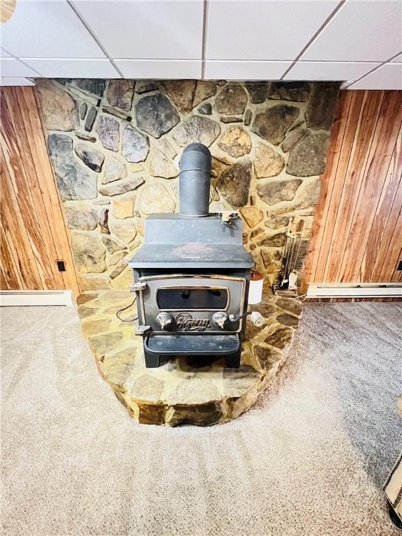 interior details with a paneled ceiling, wooden walls, carpet floors, and a wood stove