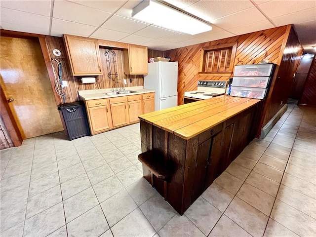 kitchen with white appliances, a drop ceiling, wooden walls, and sink