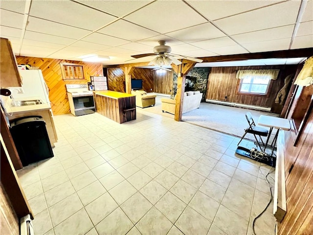 unfurnished living room with a paneled ceiling, wood walls, a baseboard heating unit, ceiling fan, and light tile patterned flooring