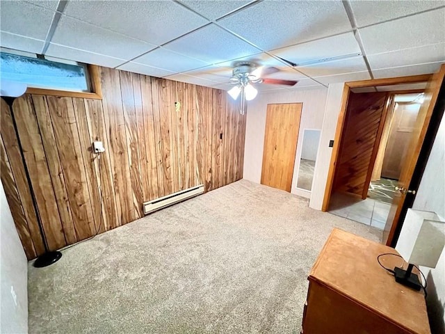 basement featuring carpet, a baseboard radiator, a drop ceiling, and wood walls