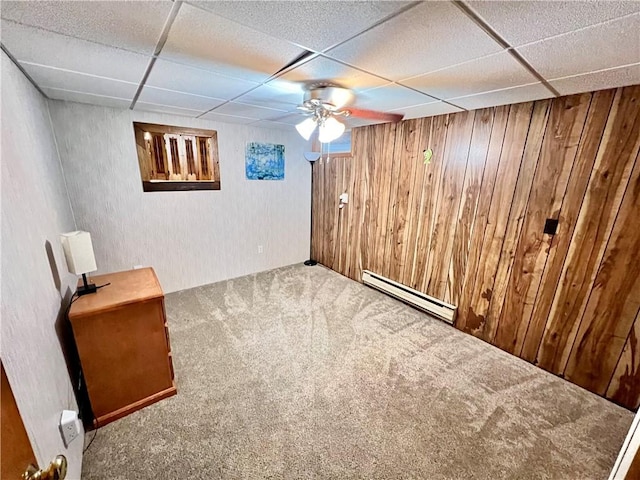 basement with carpet flooring, wooden walls, a drop ceiling, and a baseboard heating unit