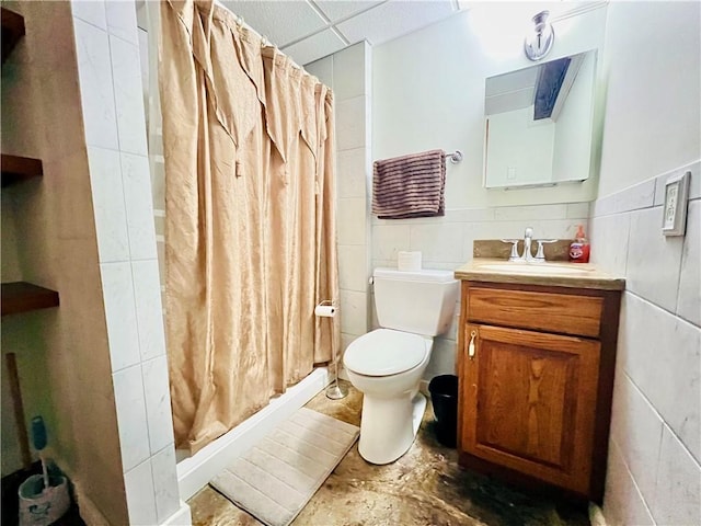 bathroom with a paneled ceiling, vanity, toilet, tile walls, and curtained shower