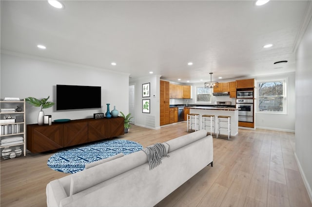 living room with crown molding, an inviting chandelier, and light wood-type flooring