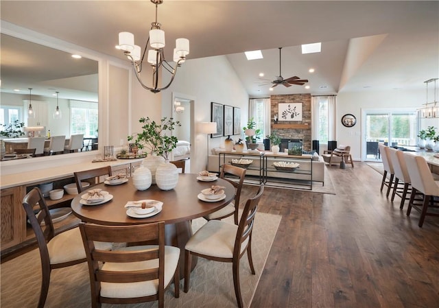 dining space with ceiling fan with notable chandelier, vaulted ceiling, a fireplace, and dark wood-type flooring