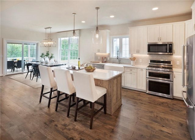 kitchen with a center island, white cabinets, sink, appliances with stainless steel finishes, and decorative light fixtures